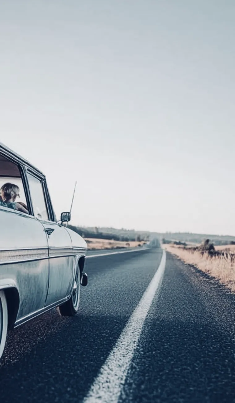 An old car on a long straight highway, seen from the side