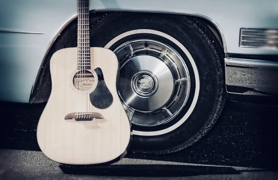 An acoustic guitar leaning against the whitewall tire of an old car